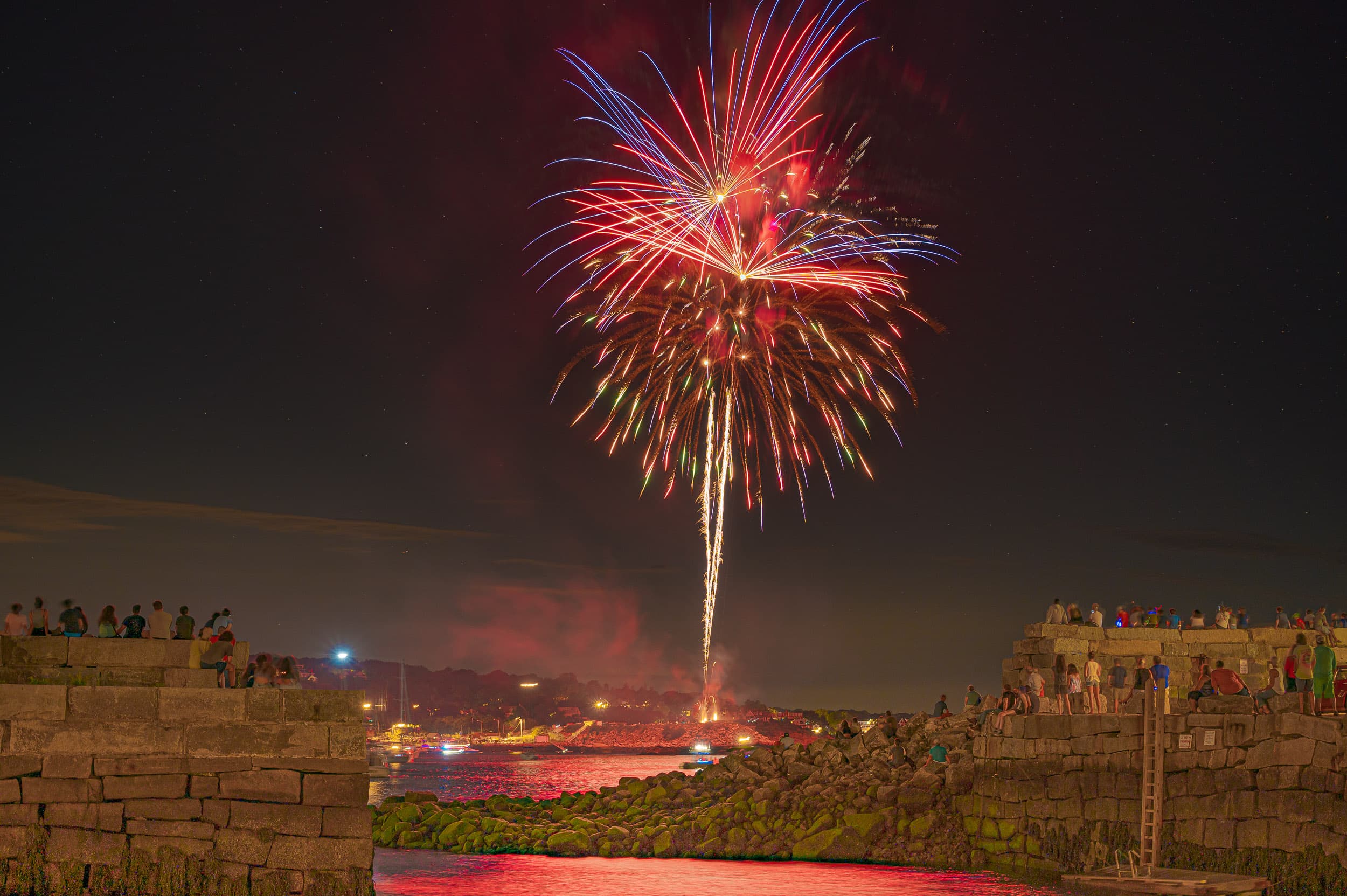 Fireworks over Rockport harbor on a summer night, breakwater crowds visible